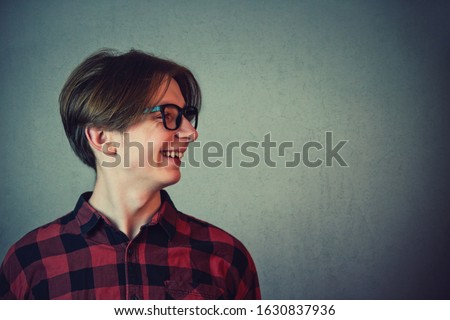 Close up side view portrait of positive boy adolescent wearing red shirt and eyeglasses looking cheerful aside isolated on gray wall background with copy space.