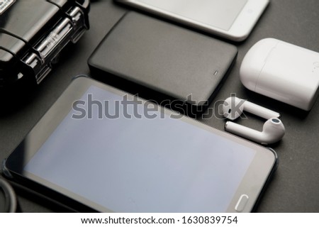 technological articles on a black background, black electronic agenda (pda), large usb memory, white wireless headphones, white headphone box, and partial telephone view and black waterproof case