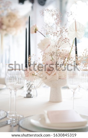 dinner table for dinner with plates, glasses and candles in a vase with roses, gypsophila and calla lilies in white and pink colors. Floral composition from a fresh bouquet for a wedding event.