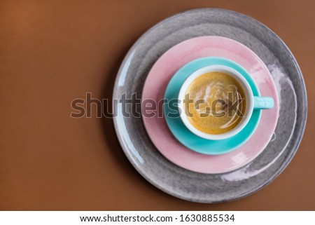 Coffee espresso in mint green cup with pink and gray plates on brown background. 