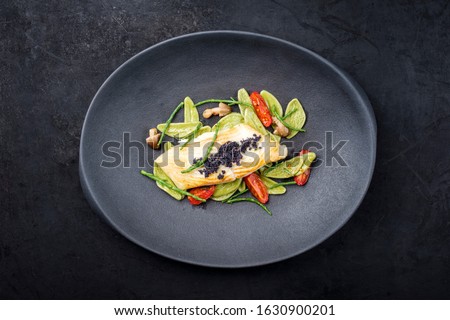 Gourmet fried Italian sea bass fish filet with spinach pasta, caviar and tomatoes as top view on a modern design plate with copy space 
