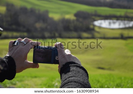 woman's hands photographing a green landscape