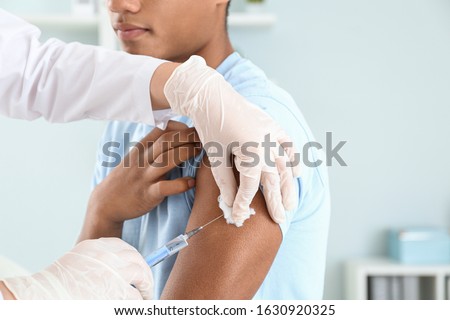Doctor vaccinating teenage boy in clinic, closeup Royalty-Free Stock Photo #1630920325