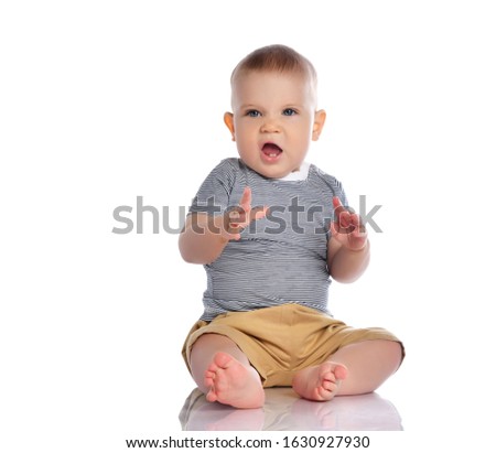 Infant baby boy in t-shirt and pants is sitting on the floor roaring like a tiger beast, playing on white background