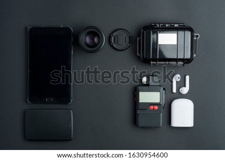 top view black photography work table, (central free space), hard disk, black tablet, camera lens, lens cover, waterproof case, digital photometer, headphones and white charger