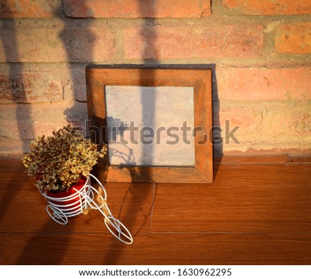 Picture frames and flower vases are placed on wooden floors, behind the brick wall, with shadows leaning over.