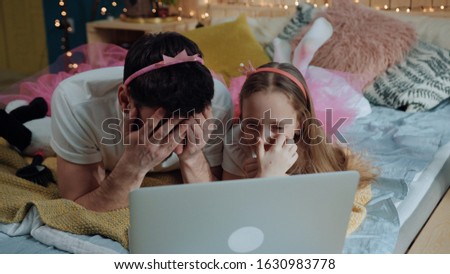Portrait of young man and girl fairies watching scary videos on laptop computer closing their faces lying on bed in girly bedroom at home.