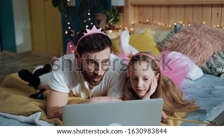 High angle side view cheerful dad and his daughter playing fairies watching cartoons having fun at home magic disney party. Funny young family holiday celebration.