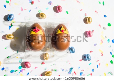 Easter chocolate  eggs party with two eggs mimiking a king and queen,  ironic easter eggs  over a white background spot painted with different color, top view, easter holiday conceptual image