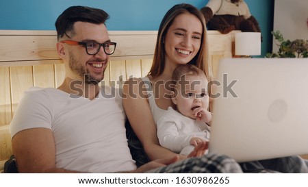 Cheerful family lying in bed in pajamas and attentively watching cartoons via laptop. Gadgets, modern style of parenting, early childhood education, baby’s development. Technology addicted. Happy