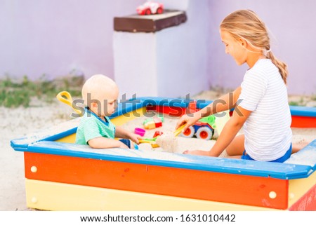 Cute baby boy playing with his sister with toys in the sandbox outdoor