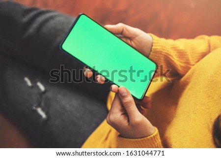 Woman using smartphone watching green screen on mobile phone, online enjoying reading social media at home close up hands