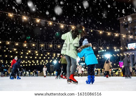 Street skating rink. Mom with daughter at the ice rink. It snows.