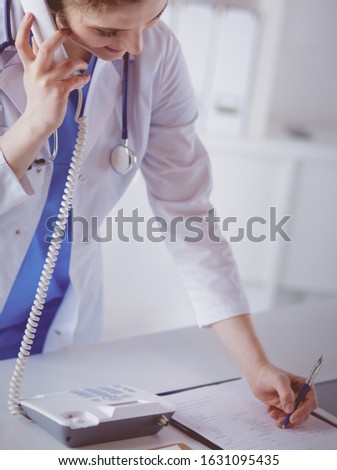 Young practitioner doctor working at the clinic reception desk, she is answering phone calls and scheduling appointments