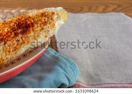 A closeup view of a plate of Mexican elote, on the left side of the frame.