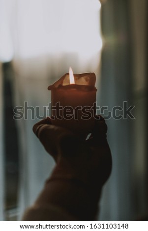 A closeup shot of a hand tightly holding a lit up candle