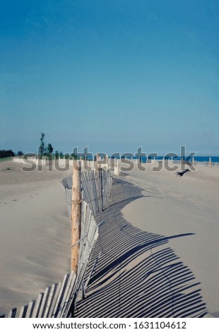 A vertical picture of fences on the beach surrounded by the sea under a blue sky