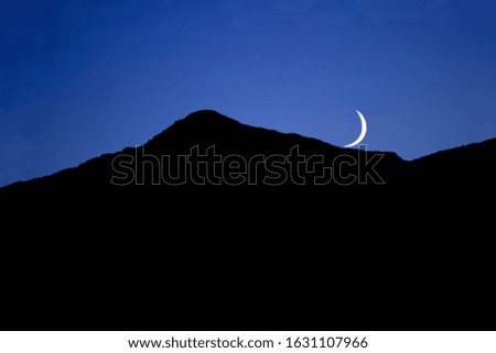 A silhouette of a hill with the moon above it on a blue sky in the evening