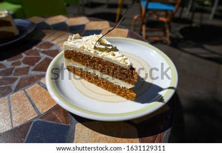 Delicious piece of carrot cake with a fork stuck in, served on a plate in a coffee shop on a sunny day.