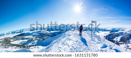 snow shoe hiker a the summit of the snowy mountain. panoramic picture of winter hiker at the top of the hill. gorgeous swiss alps mountain panorama with sun and blue sky