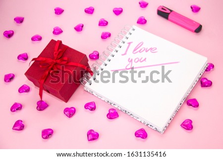 gift box with a red ribbon bow, on a pink background. Notepad for notes