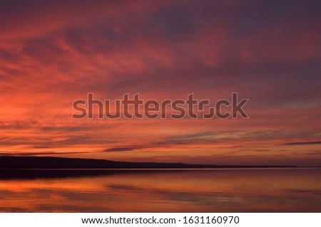 A landscape of the sea surrounded by hills under a cloudy sky during the sunset