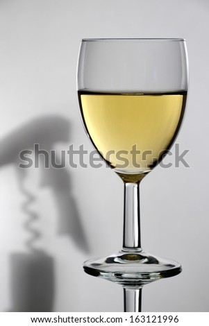 A glass of white wine with a corkscrew shadow in the background