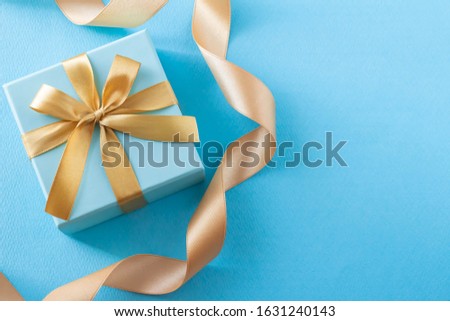 Image of sophisticated gift with blue background and gift box and gold ribbon