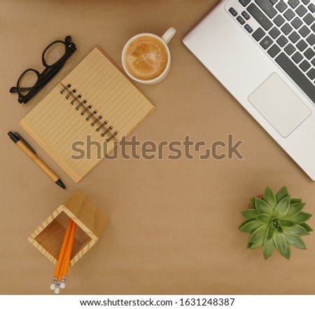 Flat lay, top view office table desk. Workspace with blank clip board, keyboard, office supplies, pencil, green plant and coffee cup on brown craft paper  background.