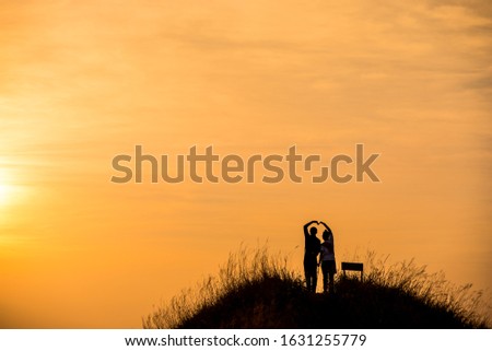 silhouette picture man and women hold one's hands with orange sky background
