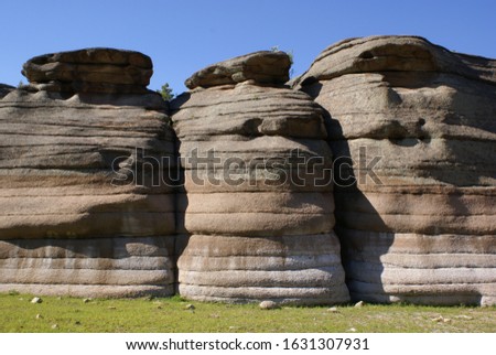 rocks that look like stacks of pancakes or pillars against a background of blue sky and green grass close up