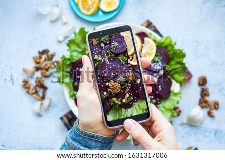 Woman take picture of vegan food with phone at her kitchen. Hand make a closeup smartphone photo of beetroot salad with walnuts for blogging or social media content. Vegetarian healthy food.