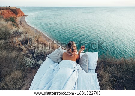 Woman drinking wine enjoying view on beach landscape while relaxing in bed on mountain in sunset on the edge of Earth. Calm and quiet wanderlust concept moment when person feels happiness and freedom. Royalty-Free Stock Photo #1631322703