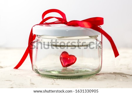 Little red heart in glass jar on white background with ribbon and copy space