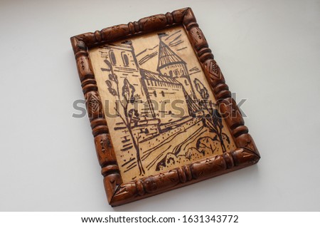 A wooden picture depicting the fortress wall and town of the city, made using the technique of pyrography. The picture is decorated with carved wooden frame and varnished.