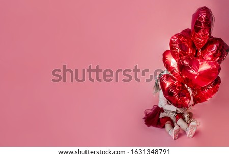 curly blond girl in a full red skirt holds a huge bunch of foil balloons in the shape of a heart on a pink plain background, suitable for inserting an inscription