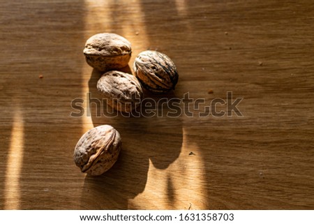 Solid and embossed brown-shelled walnuts lie on a wooden table, illuminated by the harsh sunlight