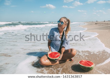 Slim girl in fashion style swimwear eating watermelon at sand beach and enjoying tropical paradise by sea. Perfect summer vacation, good vibes, vegan diet.