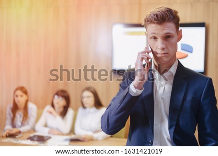 Stylish young businessman wearing a jacket and shirt on the blurry background of a working office with people talking on a mobile phone
