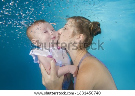 Mom with a small daughter swim underwater in a swimming pool