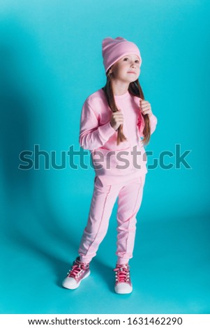 Close up portrait of little cute adorable girl in soft pink costume posing alone on blue isolated background in studio. Childhood, fashion kids, baby model concept