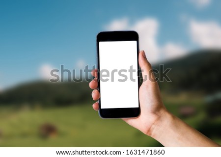 Mockup image of hand holding white mobile phone with blank white green nature background.