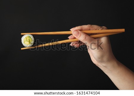 Woman holding sushi roll with chopsticks on black background, closeup