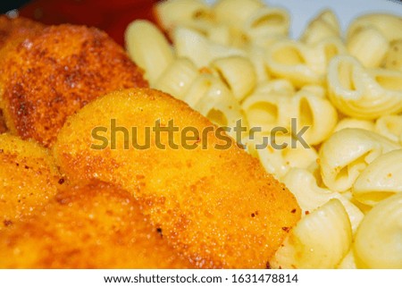 Fried chicken nuggets and cooked pasta on a plate. Close up.