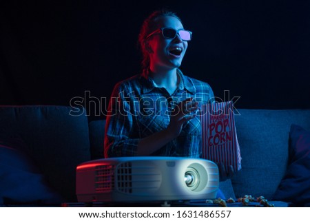 Cinema and movies in 3D. A girl looks in 3D glasses with a projector and popcorn