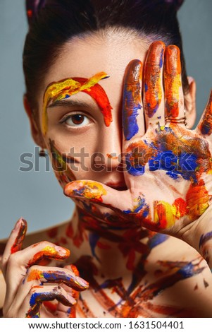 Portrait of a beautiful girl in the paint. Closeup portrait of a girl with face and hands with different paint. Fashion art concept, beauty, creative people freelance people