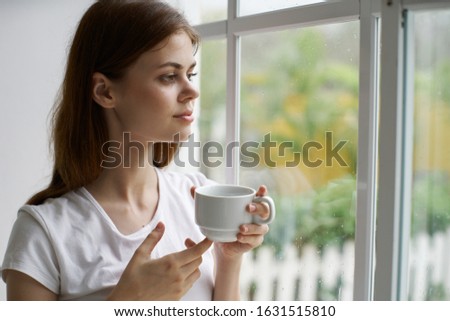A cup in the hand of a beautiful woman near the window