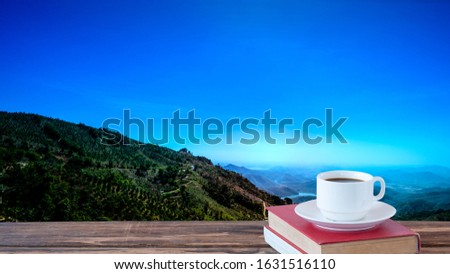 A selective focus picture of a cup of coffee and old book on wooden table with mountainous landscape background