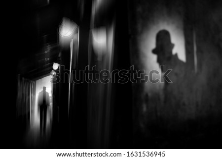 Silhouette of a man in a coat and hat in a dark alley on a rainy night. theme of violence and cruelty. blur effect Royalty-Free Stock Photo #1631536945