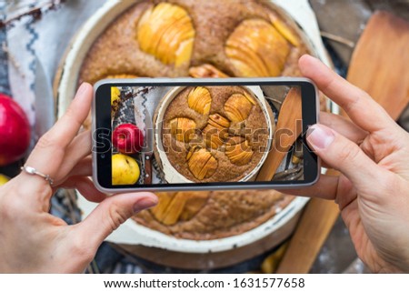 Woman take a picture of apple pie or cake using phone at her kitchen. Vegan healthy dessert. Smartphone food photography